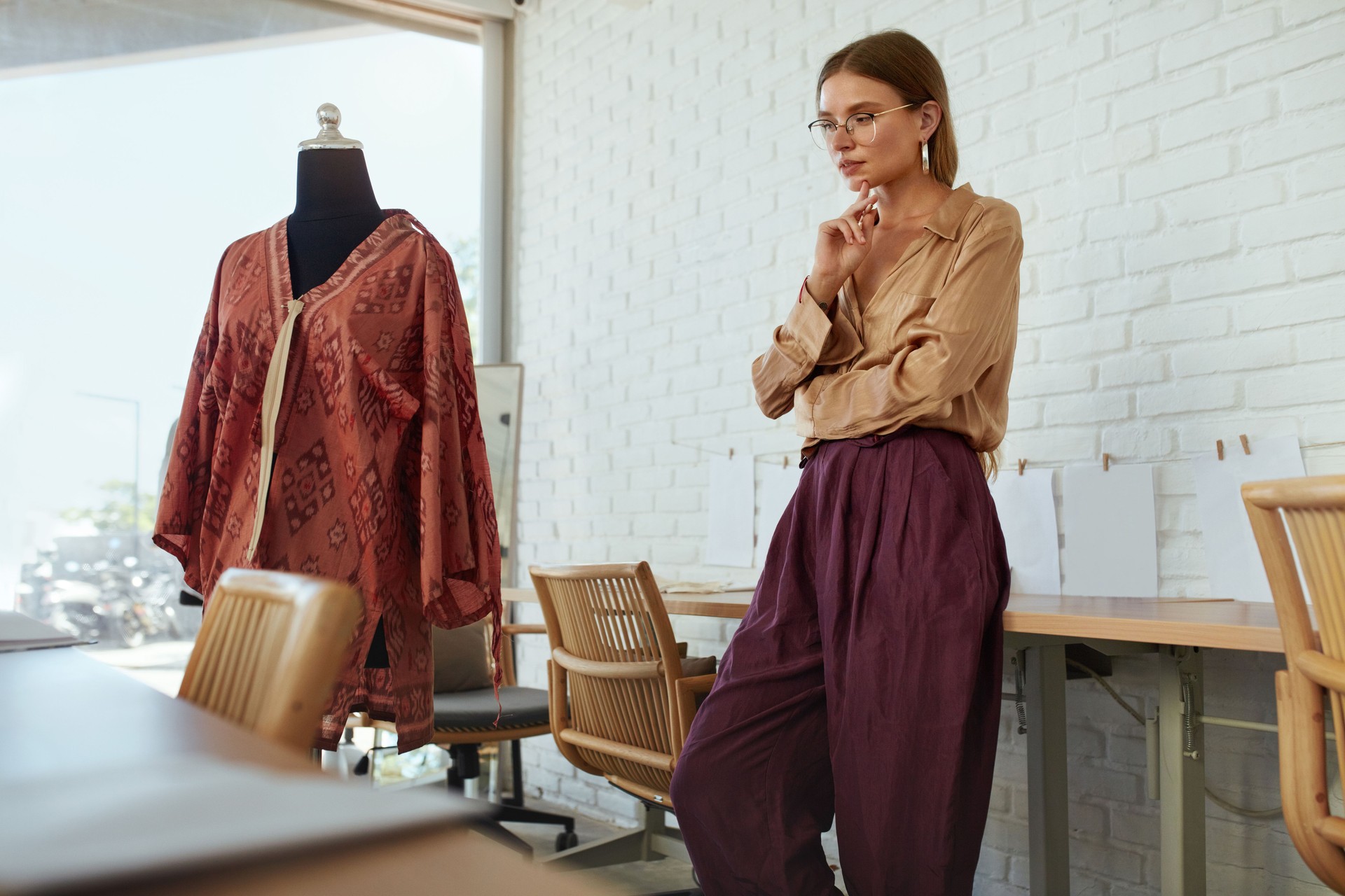 Workshop. Fashion Designer Working At Atelier. Beautiful Dressmaker In Elegant Clothes Standing Near Mannequin And Thinking. Happy Woman Tailor In Glasses Near Fashionable Dress On Dummy.