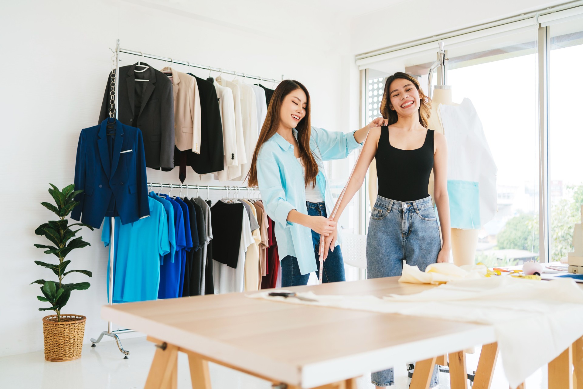 Two women interact in a bright fashion studio, surrounded by colorful clothing, showcasing creativity and style.